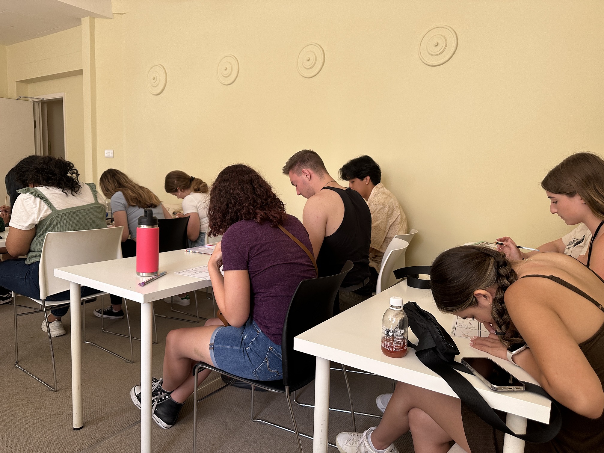Students seated at long desks are leaned over drawing on a comic strip